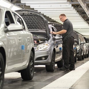 man checking cars on an assembly line in a manuracturing plant